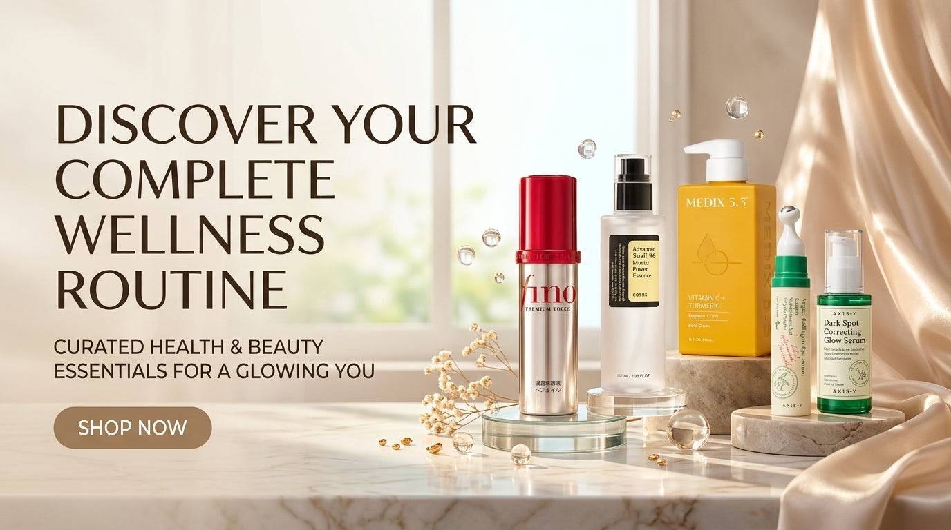 A wellness and beauty product bundle displayed on a marble surface in front of a bright window, with draped satin fabric on the right. The products include a red-capped serum bottle, a black pump bottle, a yellow box, and two smaller green and white bottles.